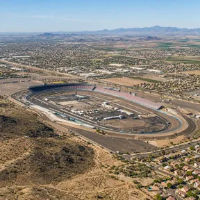 Aerial drone view of Phoenix Raceway's oval track in Avondale, Arizona, surrounded by desert and West Valley suburbs.