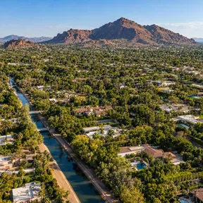 Aerial drone view of Arcadia, Arizona, showing a lushly landscaped irrigation canal neighborhood with Camelback Mountain in the background.