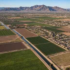Aerial drone view of irrigated farm fields and a canal bordering a neighborhood in Laveen, Arizona.